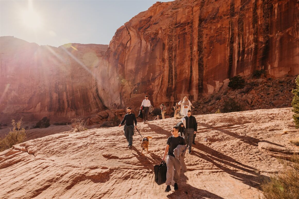 Elopement guests hiking rocky trail to Corona Arch for Moab wedding ceremony