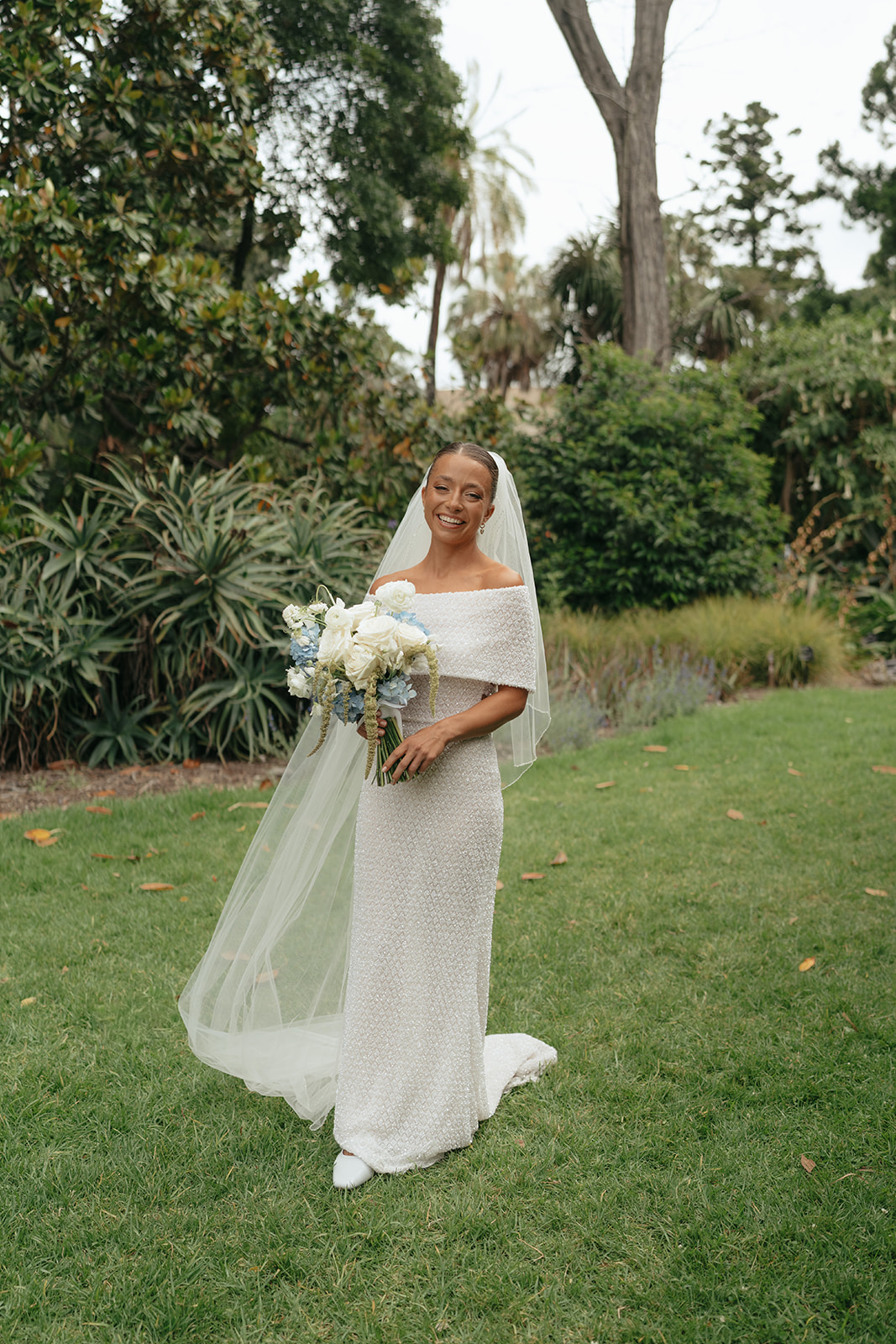 Bride in strapless Rosa Clara gown holding blue and white bouquet with fruity florals at garden wedding