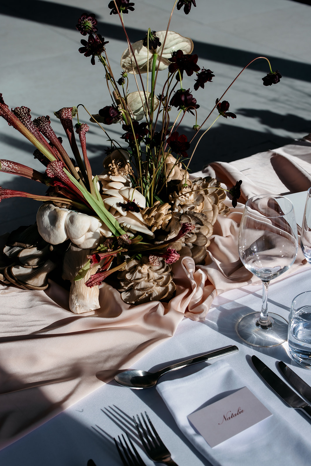 Close-up of a unique wild mushroom and sarracenia pitcher plant wedding reception centrepiece with dark burgundy florals and oyster mushrooms on a blush silk tablecloth at Marnong Estate Winery, florals by The Beautiful Bunch, photography by Kinship by Kristy