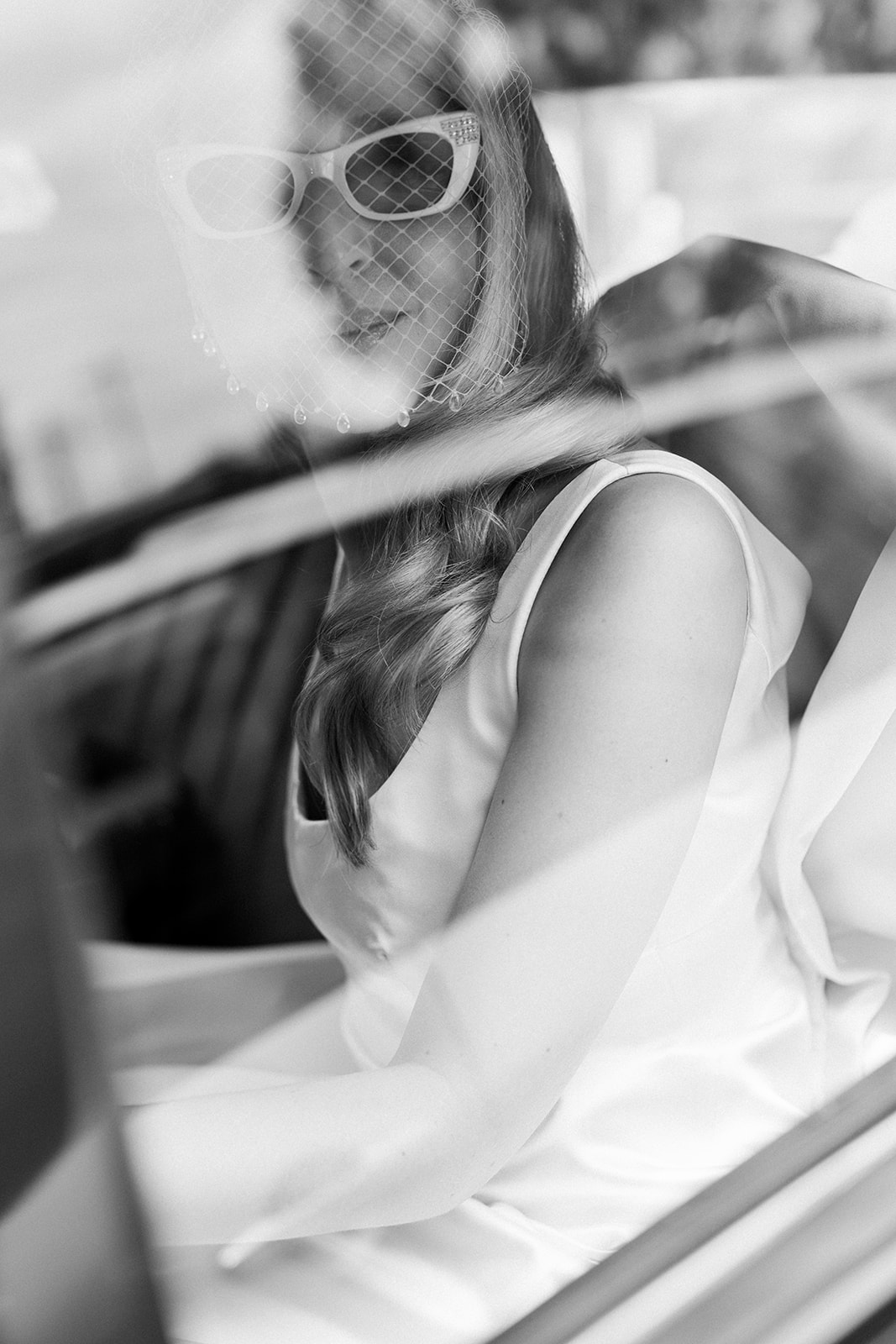 Black and white candid of bride wearing white cat-eye sunglasses and custom silk gown travelling to her Melbourne church wedding ceremony – photography by Kinship by Kristy